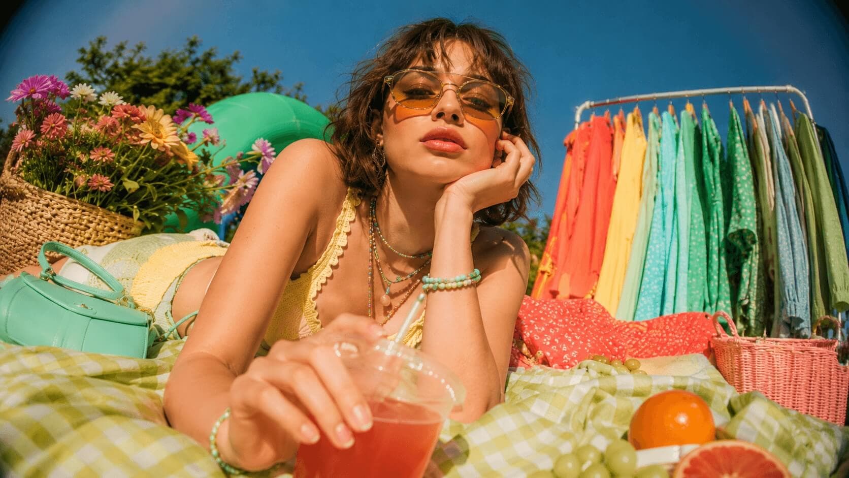 A sunlit picnic scene with a rail of clothes in every colour of the rainbow, from coral through yellow, green and teal